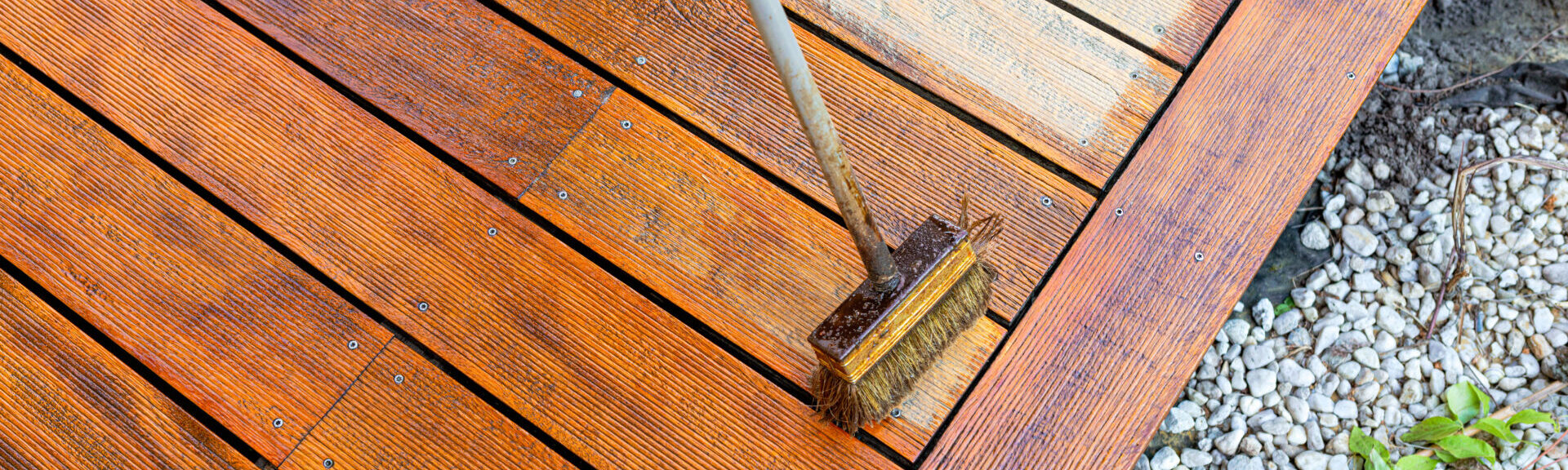 Close Up Of A Wooden Deck Being Stained With A Brush For Protection And Maintenance During A Home Improvement Project In Bright Sunlight